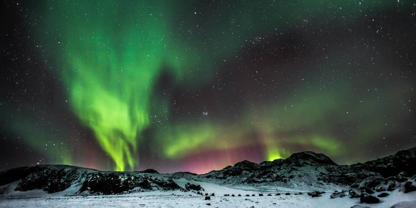 Green aurora with pink fringes over snowy jagged mountains
