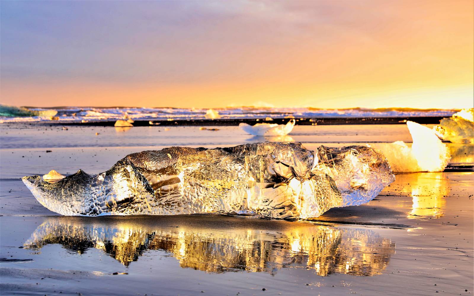 Clear block of glacier ice on black sand at sunset, Diamond Beach