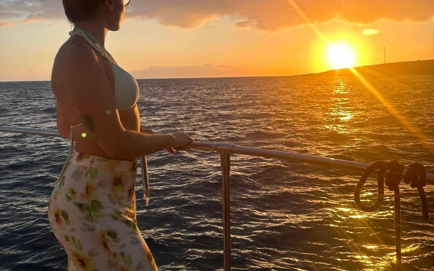 Woman at a boat rail at sunset, golden sun on the water