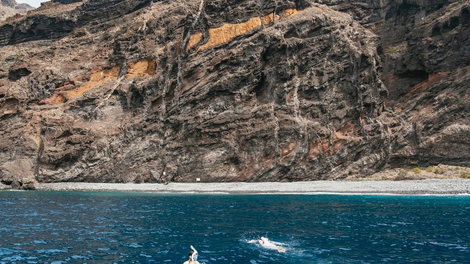 Ochre and grey volcanic cliff face close-up from the sea, layered rock