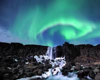 Green aurora over a small waterfall between dark lava cliffs