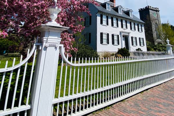 A white picket fence and a black colonial house behind it