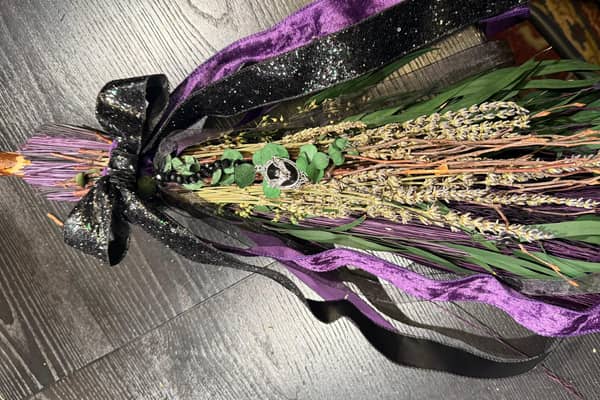 A finished besom bound with purple and black ribbon and feathers