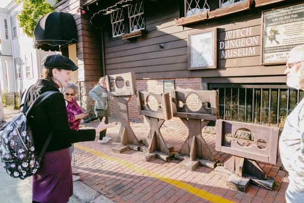 A guide in a black tricorn hat beside a display of wooden stocks