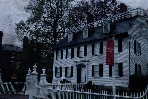 A long white clapboard mansion behind a fence on a bare-tree street