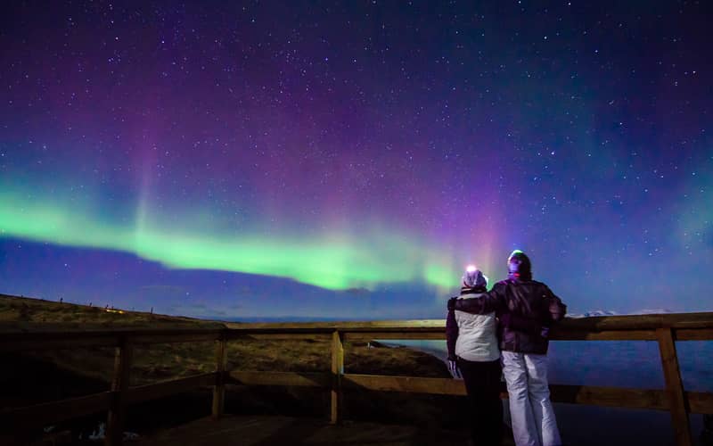 Couple at a wooden fence under a purple and green aurora, starry sky