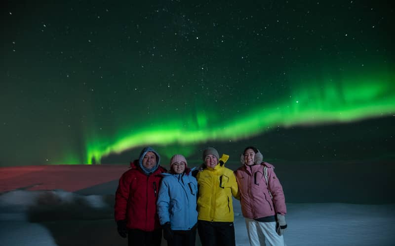 Four guests in colourful jackets posing for a guide photo under aurora