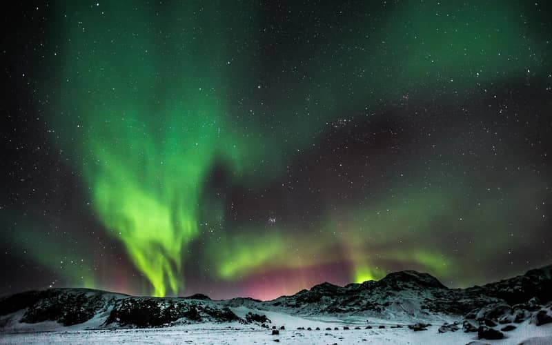 Green aurora with pink fringes over snowy jagged mountains