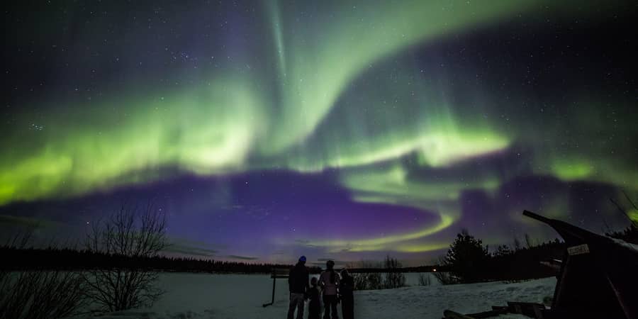 green aurora arcs with a violet lower edge over a frozen lake, tiny figures