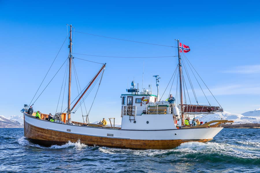 Ein weiß-hölzernes Fischerboot mit norwegischer Flagge auf tiefblauem Wasser