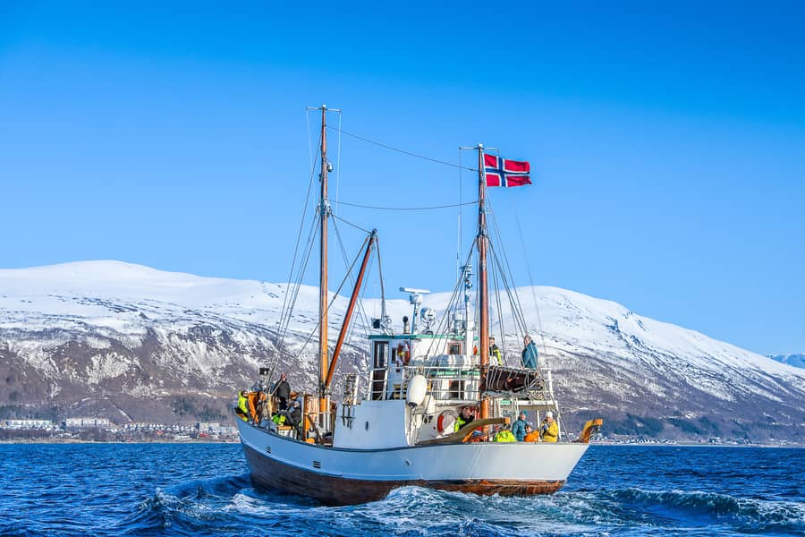 A wooden boat with a Norwegian flag below white mountains