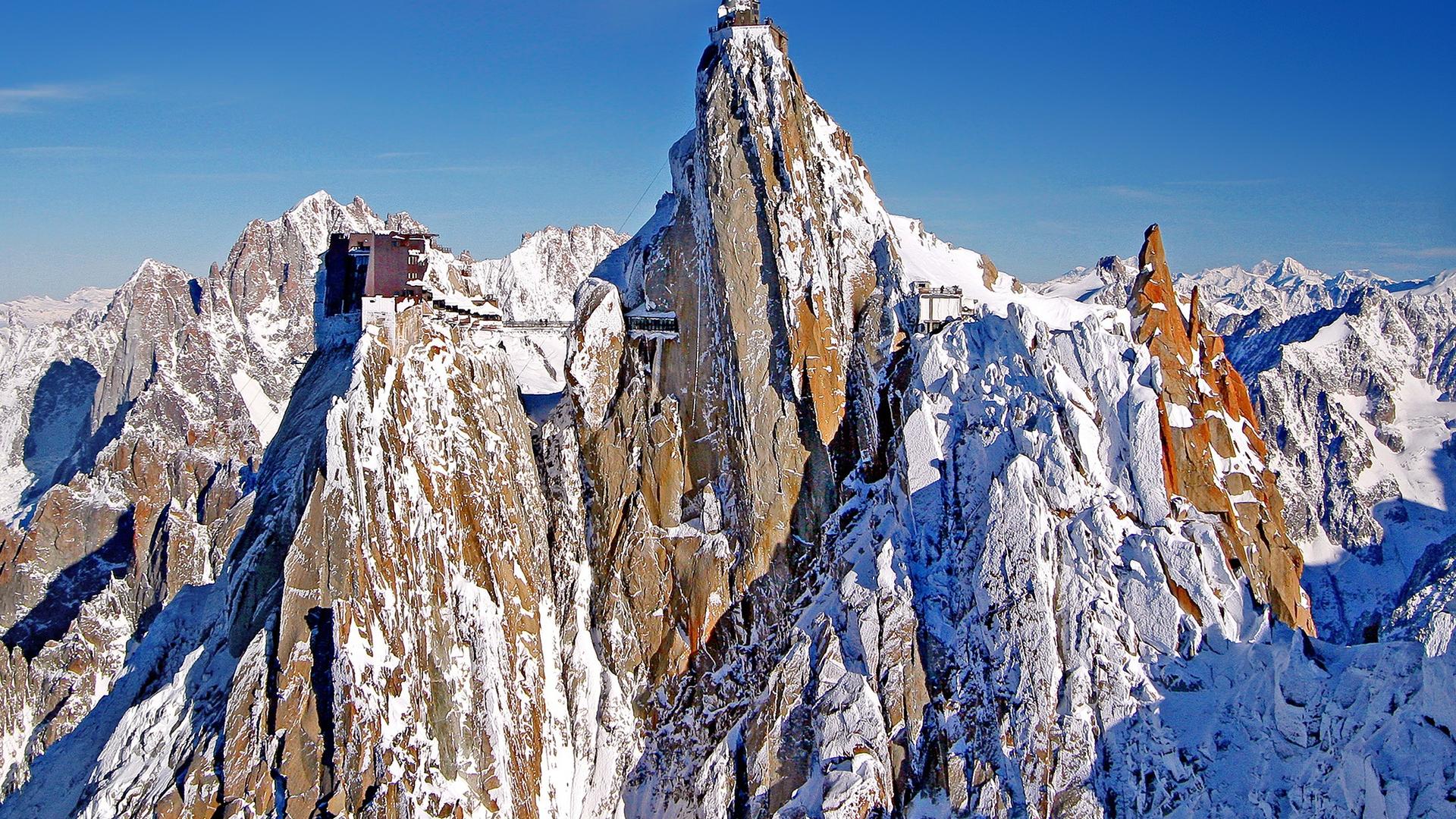 Aiguille du Midi: station on the rock, antenna, sharp red-grey ridges in snow, from a high vantage point