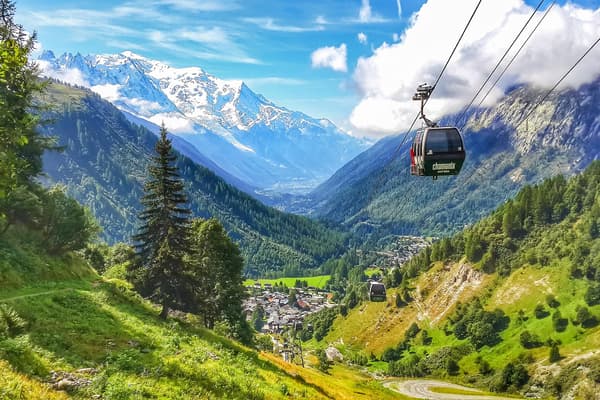 Cabina de teleférico sobre el verde valle de Chamonix en verano: bosque, el pueblo abajo, picos nevados en el horizonte