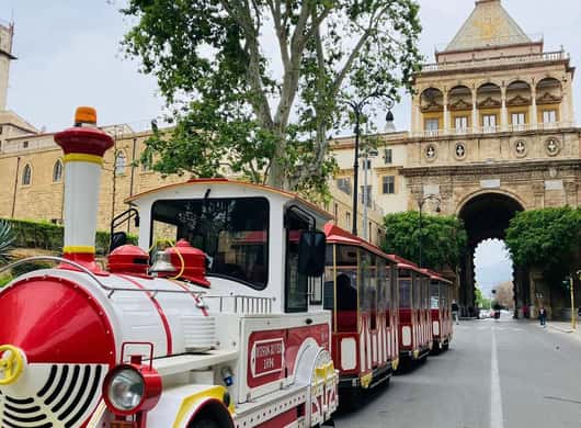 Treintje dat langs een kerk en historische gebouwen in Palermo rijdt