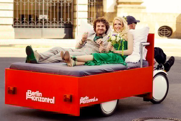 Couple enjoying a unique BedBike sightseeing tour in Berlin with historic architecture in the background. Couple enjoying a unique BedBike sightseeing tour in Berlin with historic architecture in the background.