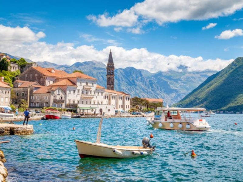 Aerial view of a speedboat on the turquoise Bay of Kotor in Montenegro with mountains and a medieval town Aerial view of a speedboat on the turquoise Bay of Kotor in Montenegro with mountains and a medieval town