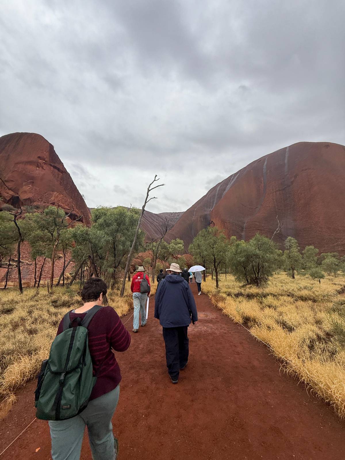 Walkers on a track at the base of the rock on a cloudy day