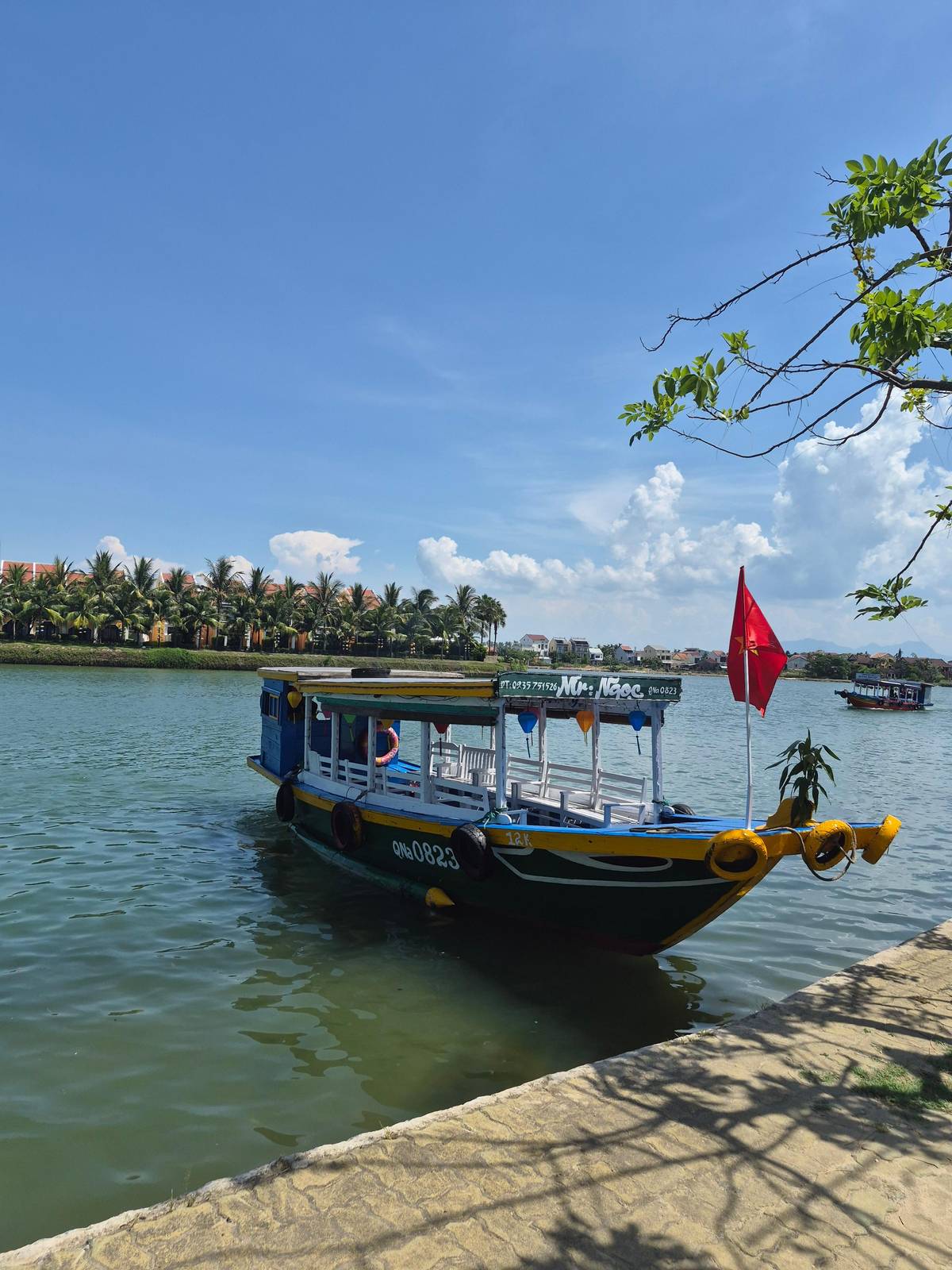 Un barco de madera con bandera roja amarrado en el río Thu Bon