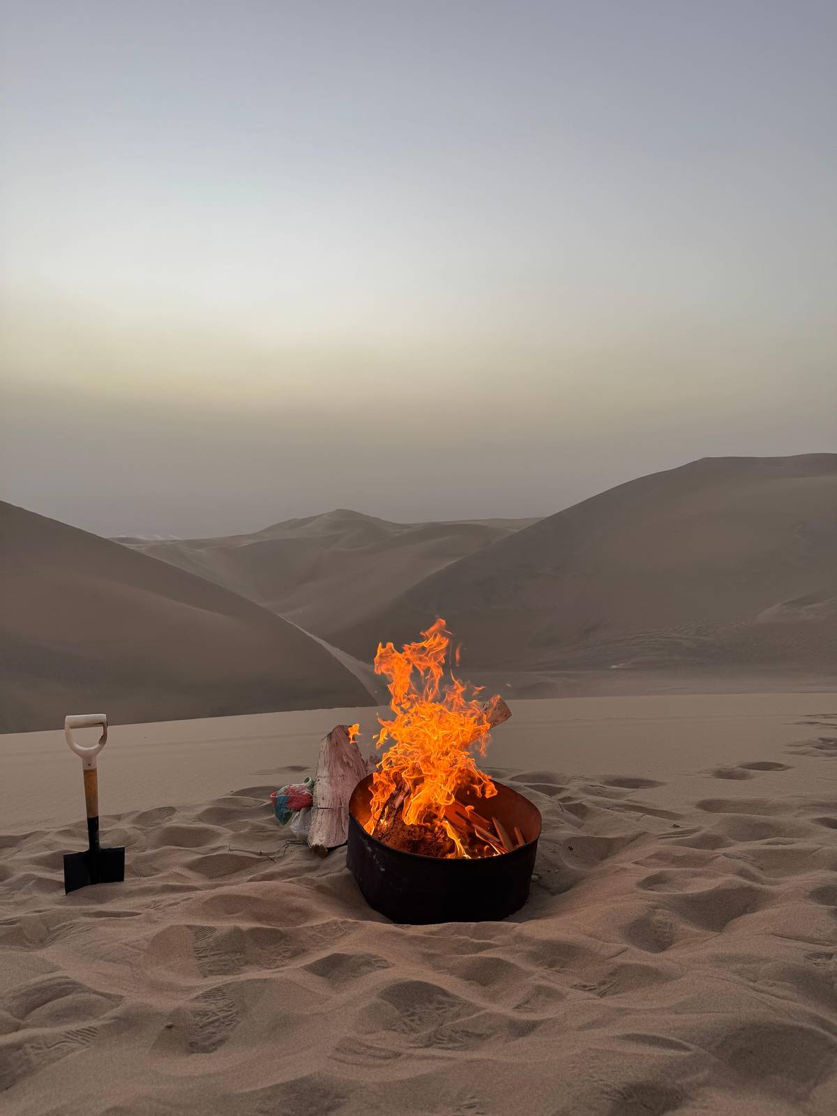 A bonfire burning in a fire pit on a dune at dusk