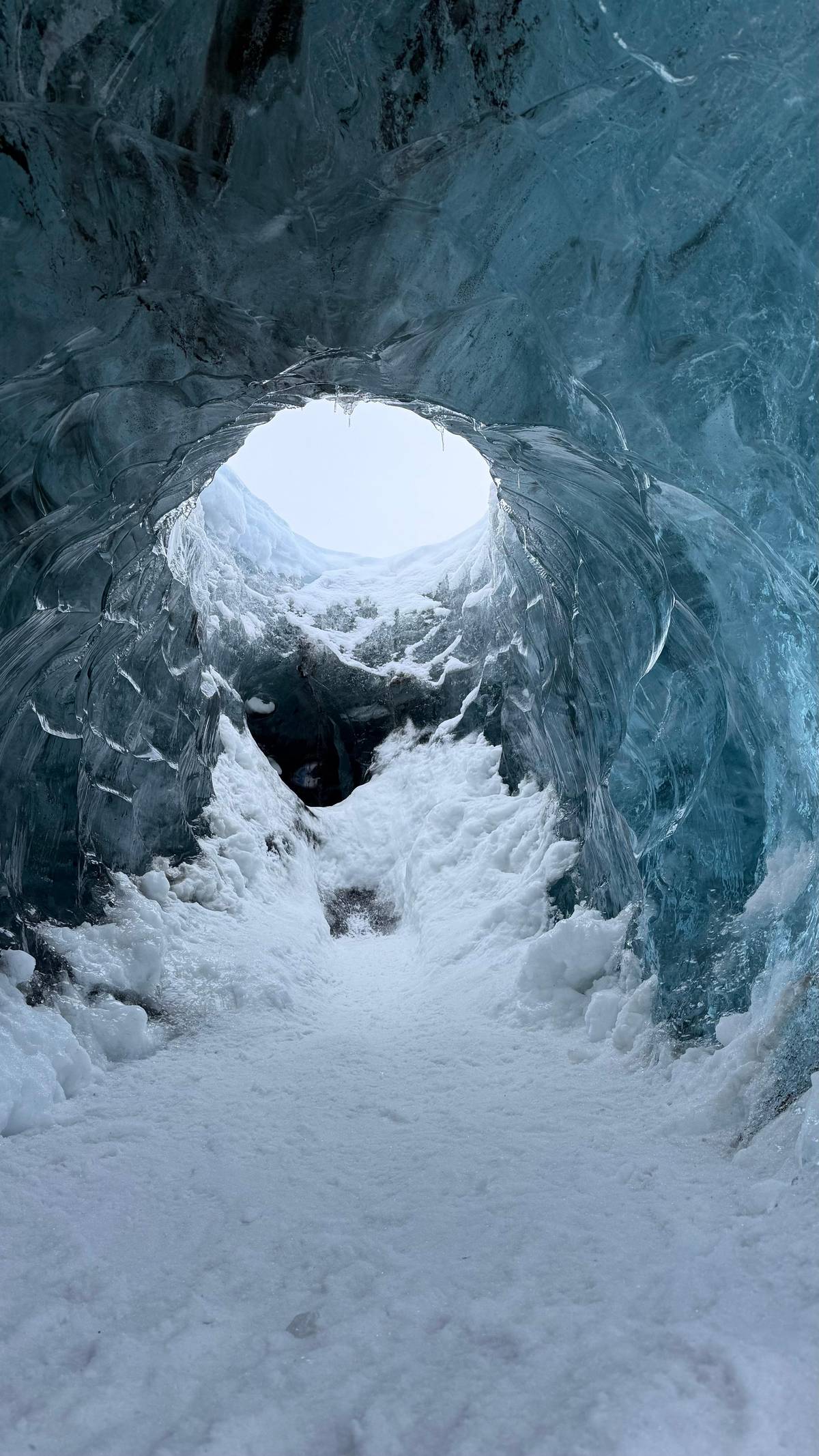 A snow-floored ice tunnel with a round skylight