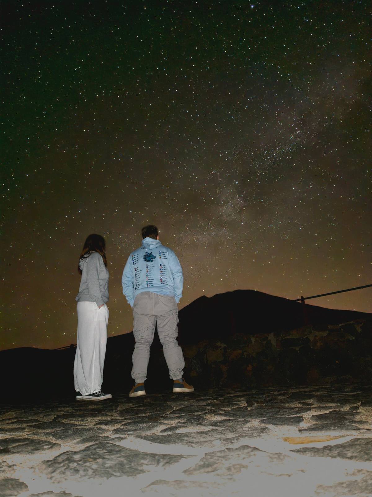 Two people looking at a starry sky on a rocky viewpoint