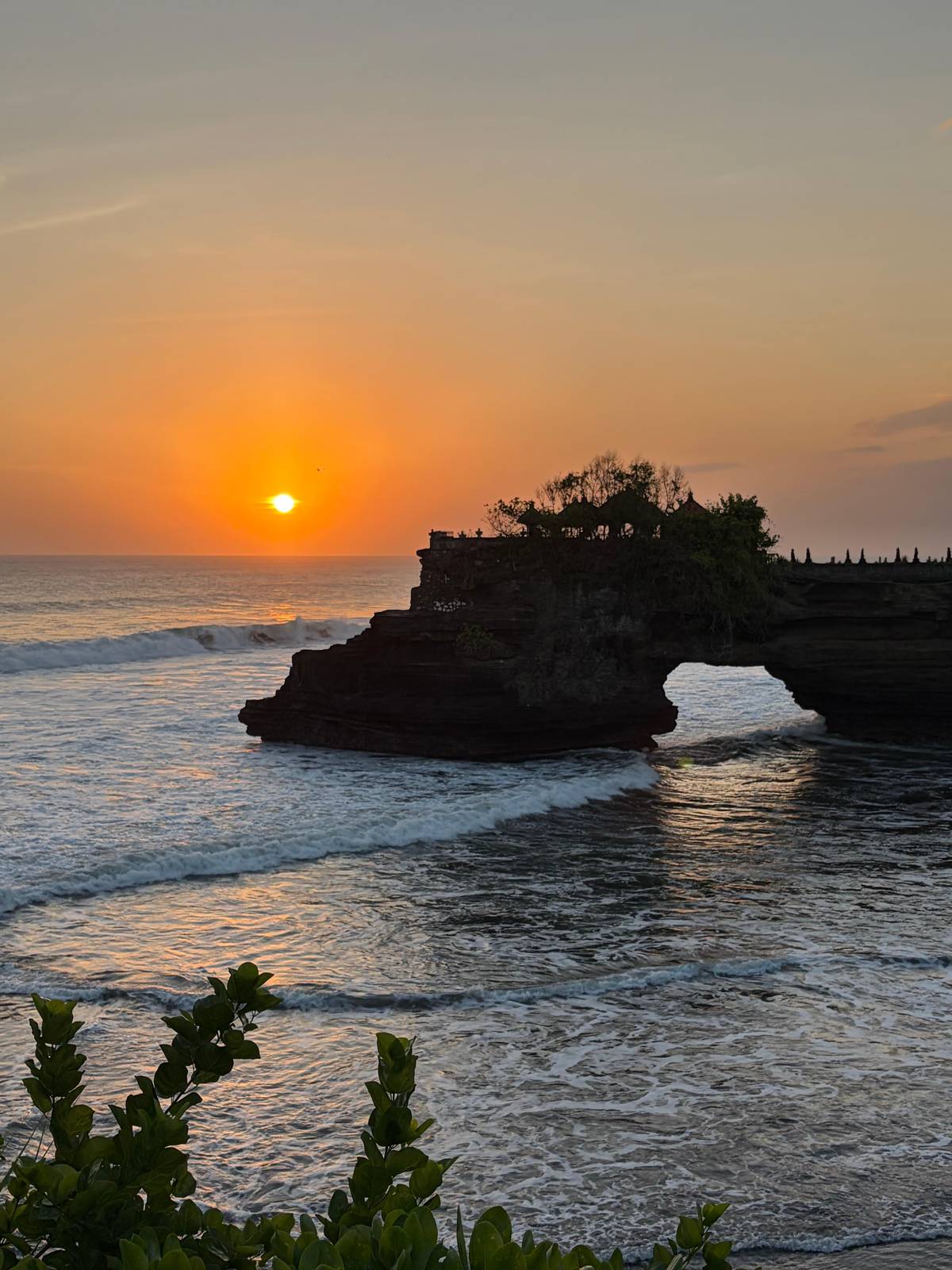 The sun setting behind the arch of Batu Bolong