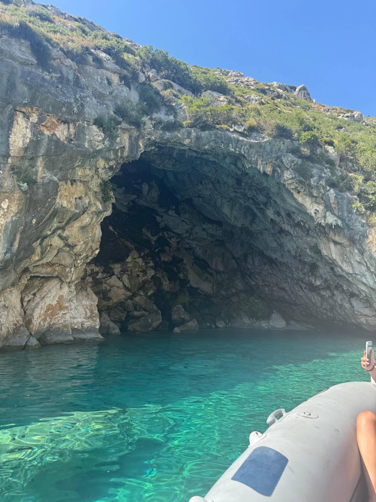 A sea cave's mouth above clear green water, seen from the speedboat