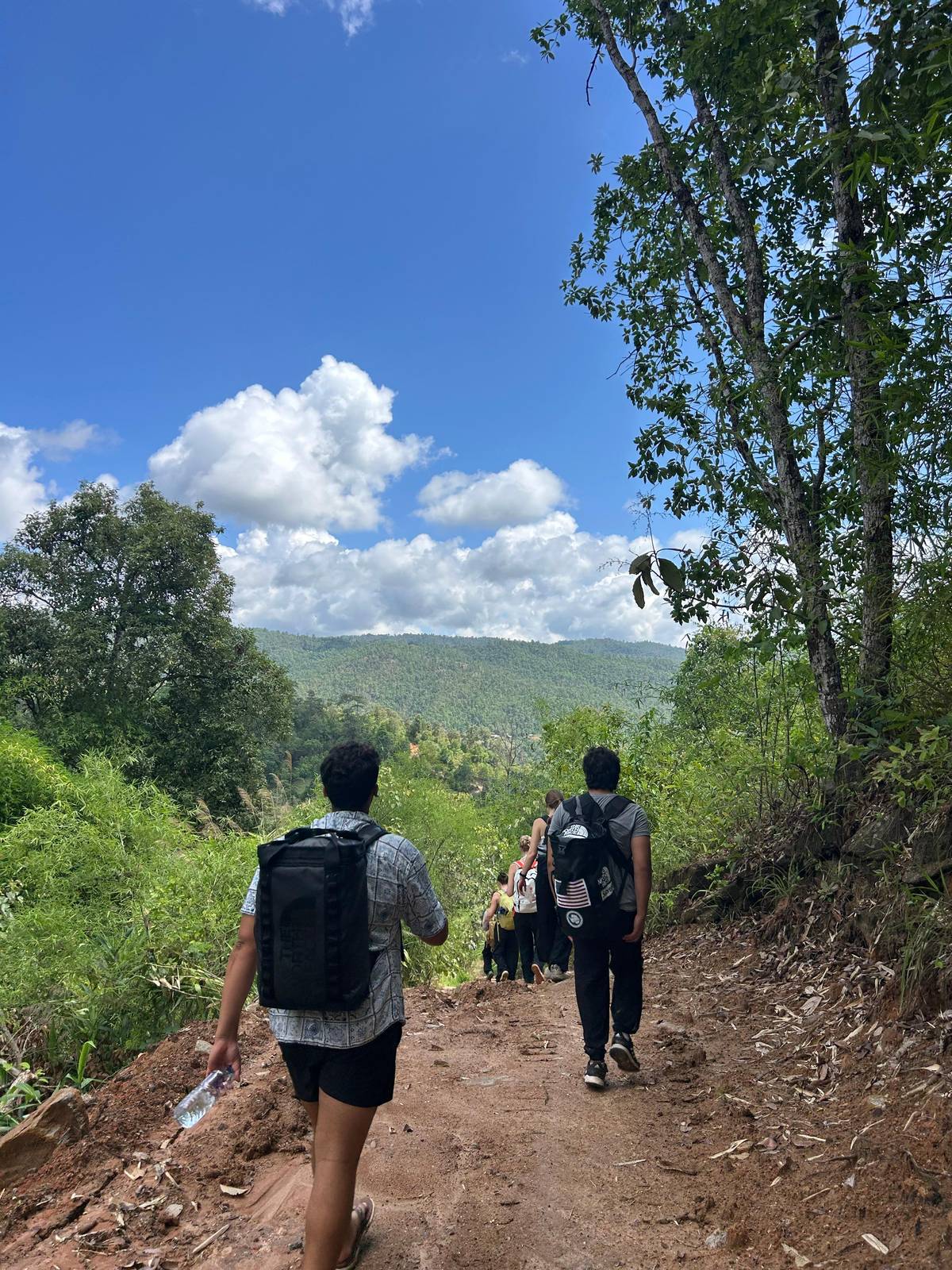 Two trekkers with daypacks walking a dirt path towards green hills