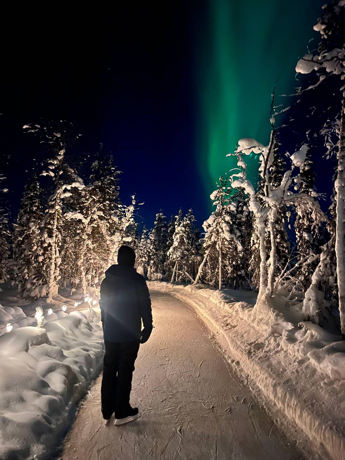 A skater on the lit trail with the aurora above the trees
