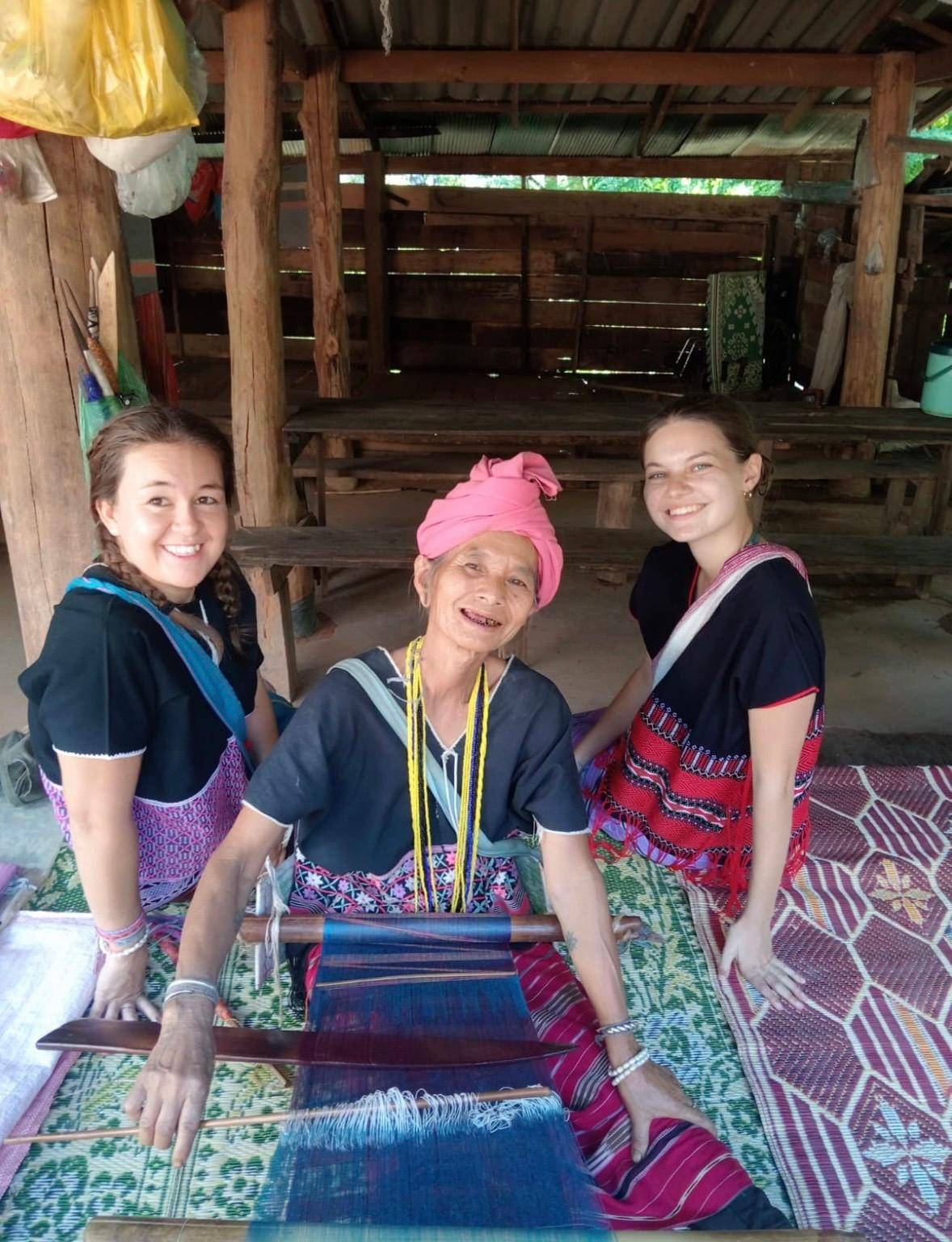 Two travellers sitting with a Karen woman at her weaving loom