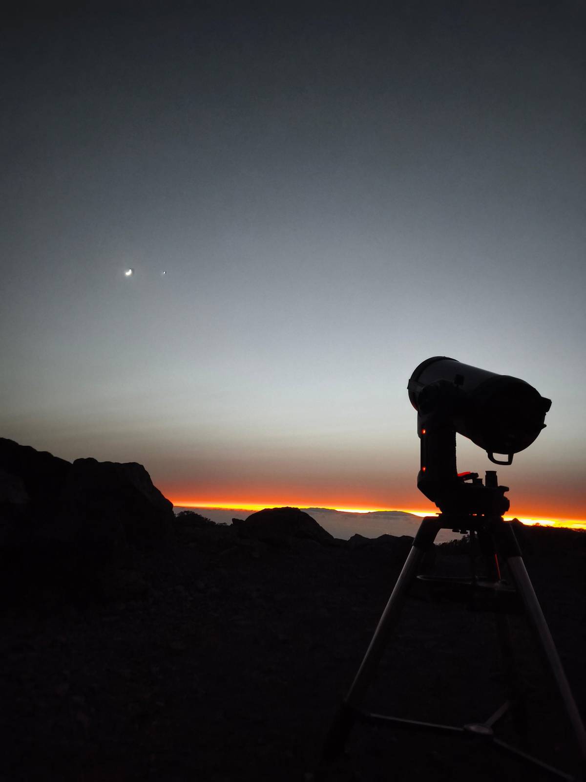 A telescope on a tripod at dusk with the horizon glowing