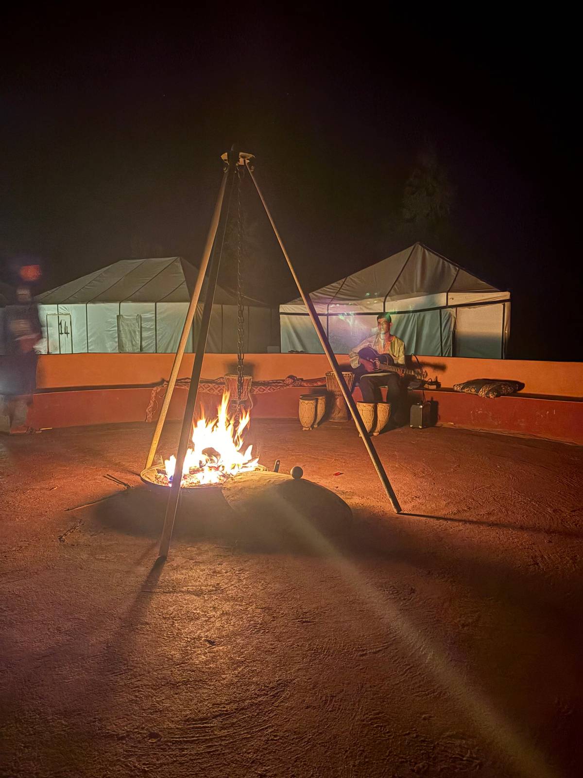 A campfire burning between tents after dark