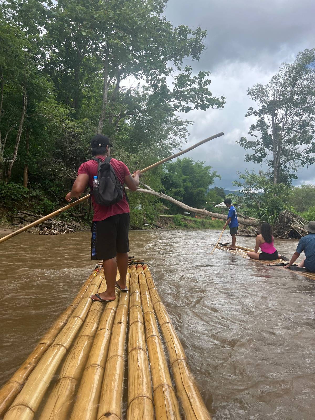 A guide poling a bamboo raft down a brown river