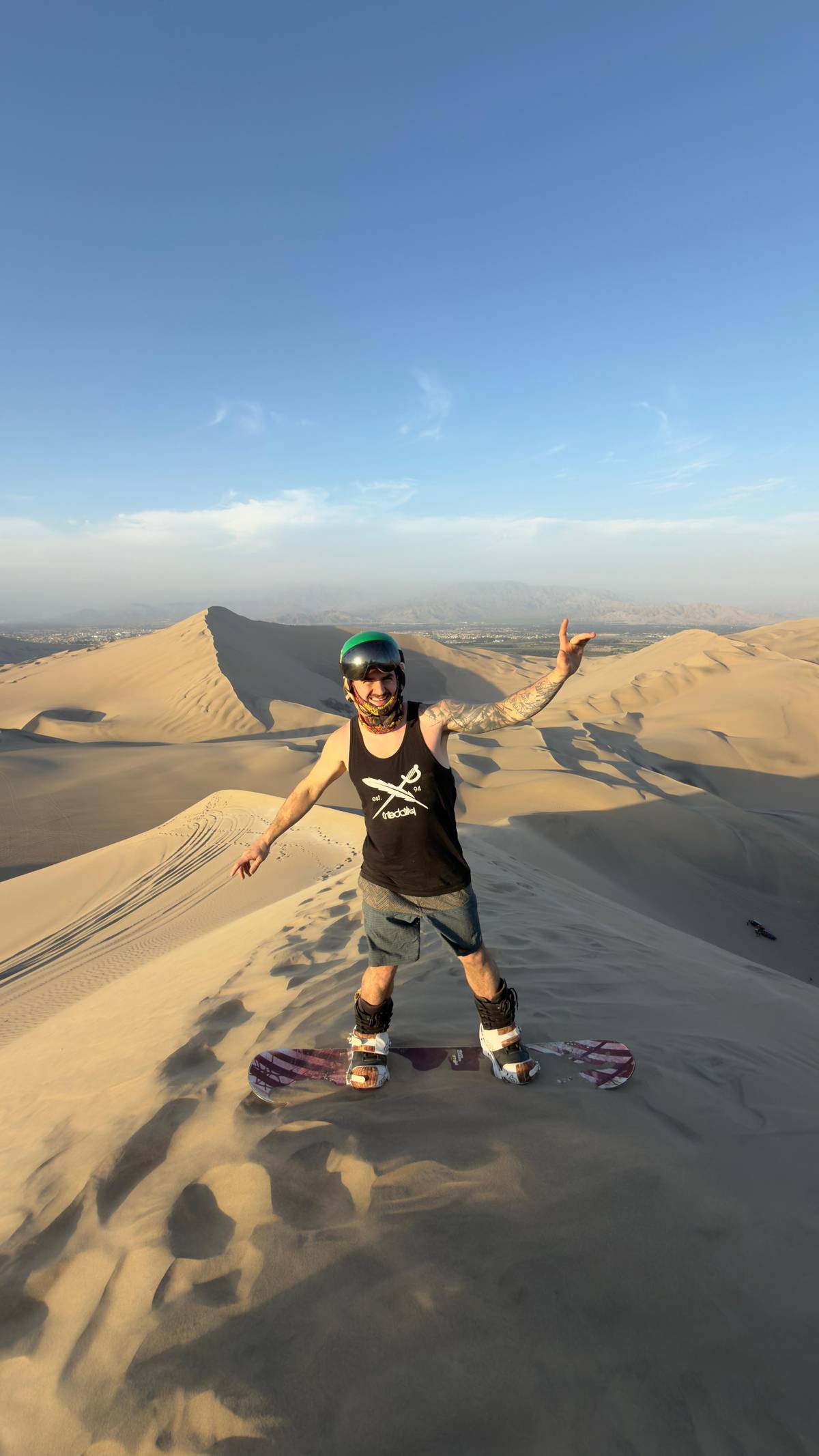 A sandboarder balancing on a ridge of pale dunes