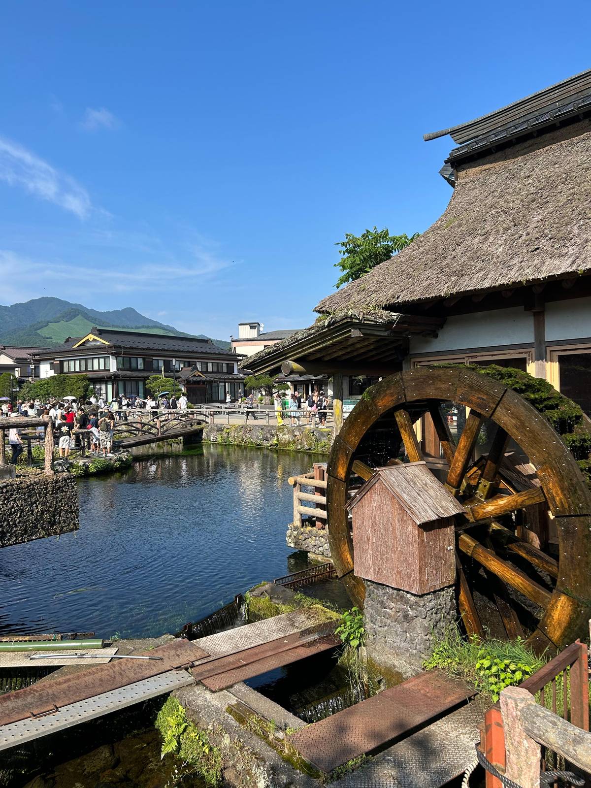 A wooden water wheel beside a clear pond at Oshino Hakkai
