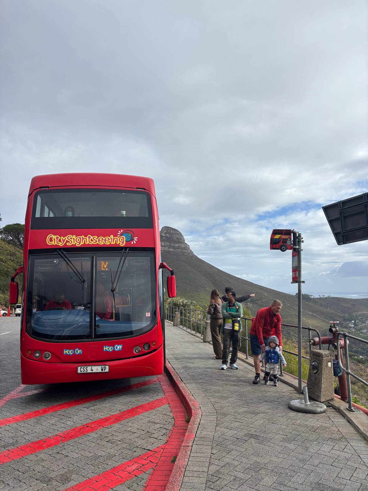 A red double-decker bus at a stop below Lion's Head