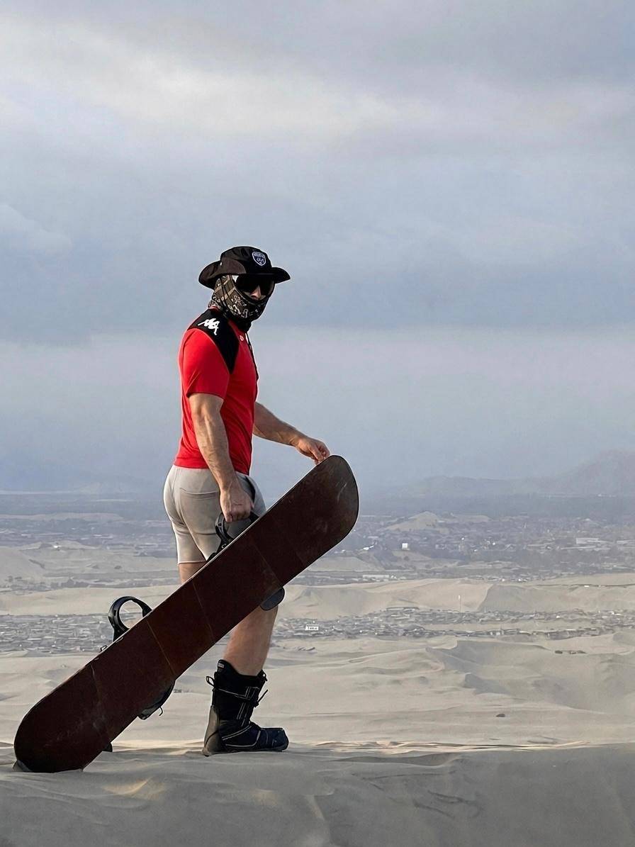 A rider holding a sandboard on a dune top high above Ica