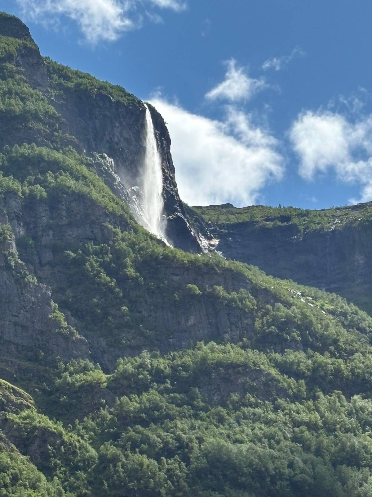 A tall waterfall pouring off a cliff above the fjord