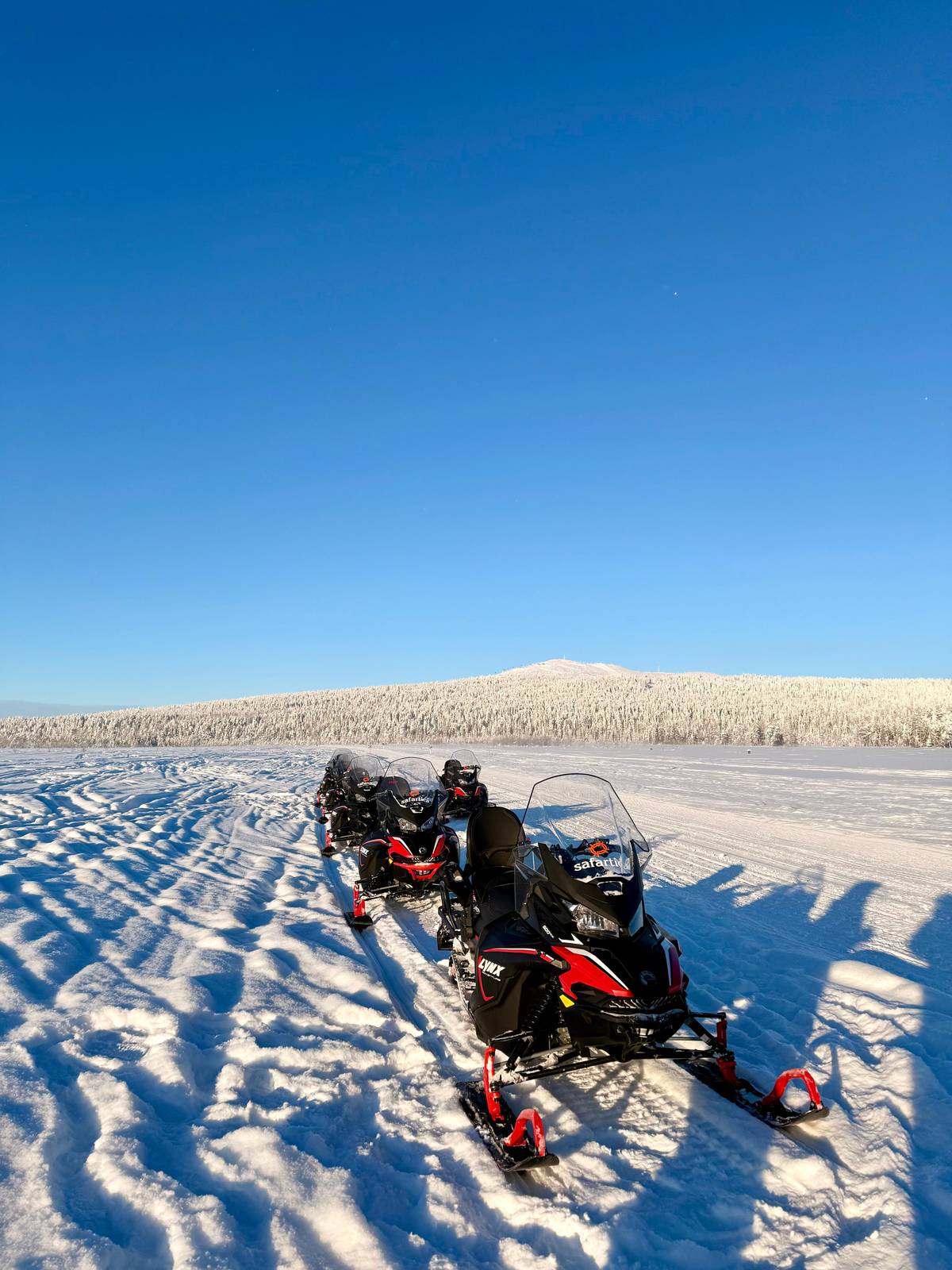 Snowmobiles crossing a frozen lake towards a low fell under a blue sky