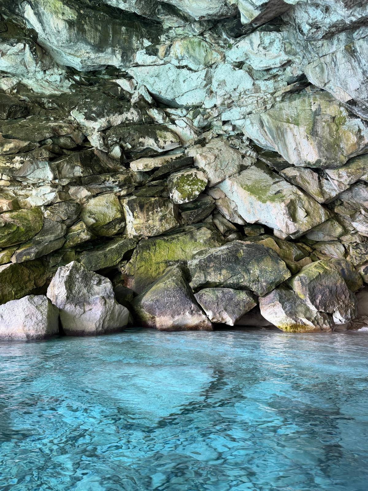 Clear water over pale boulders at the foot of a cave