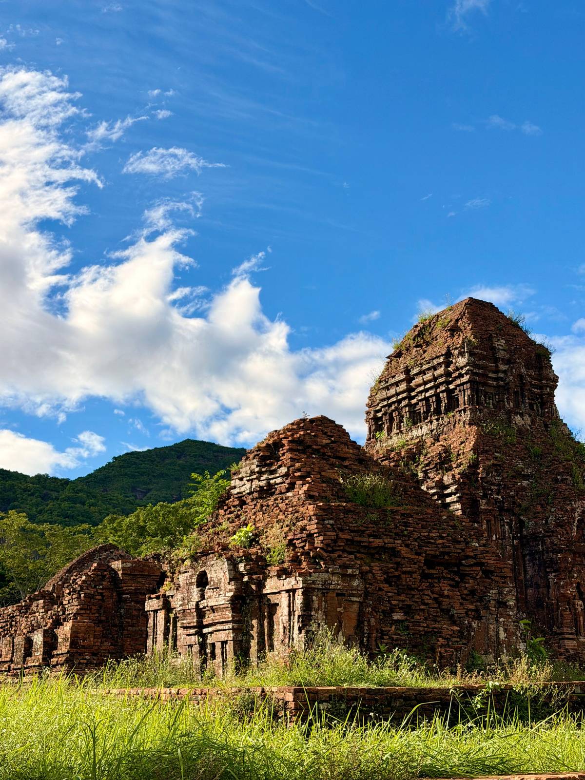 Ruinas de torres de ladrillo bajo un cielo azul con colinas boscosas detrás