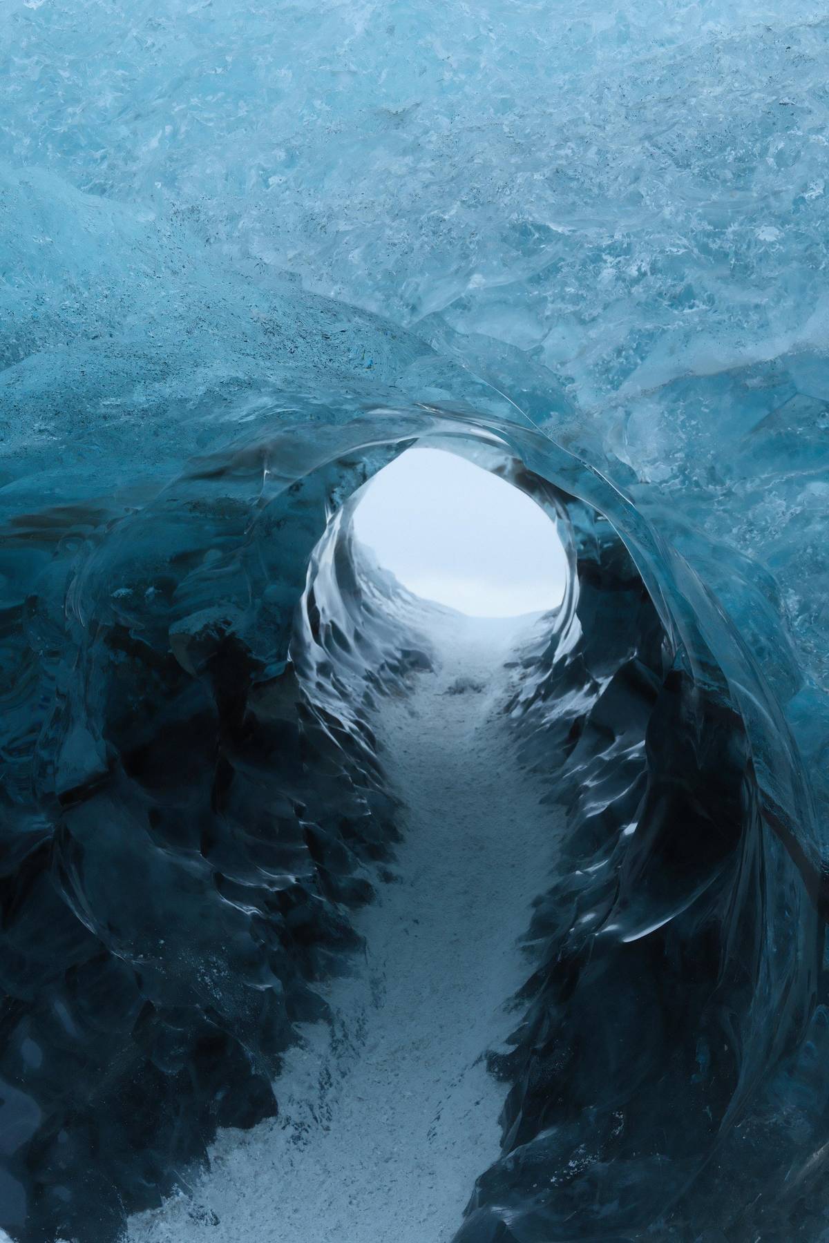 A blue ice tunnel with daylight at its far end