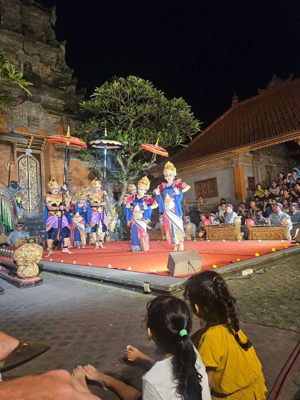 Dancers in gold costumes on a stage before a carved gate at night