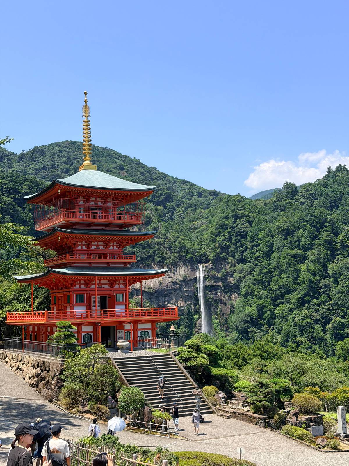 A vermilion three-storey pagoda with Nachi Falls behind