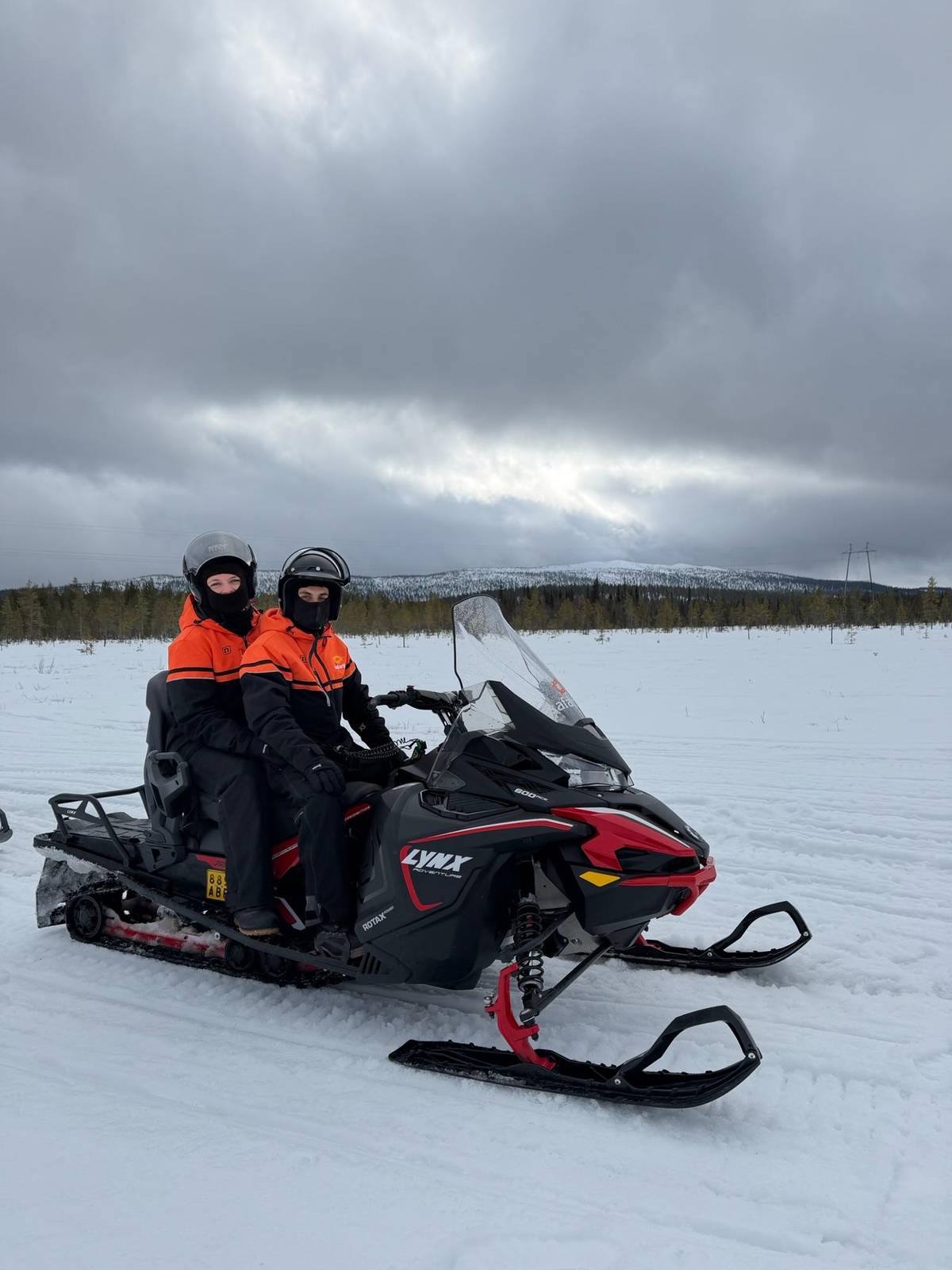 Two riders on a red and black snowmobile on a groomed track