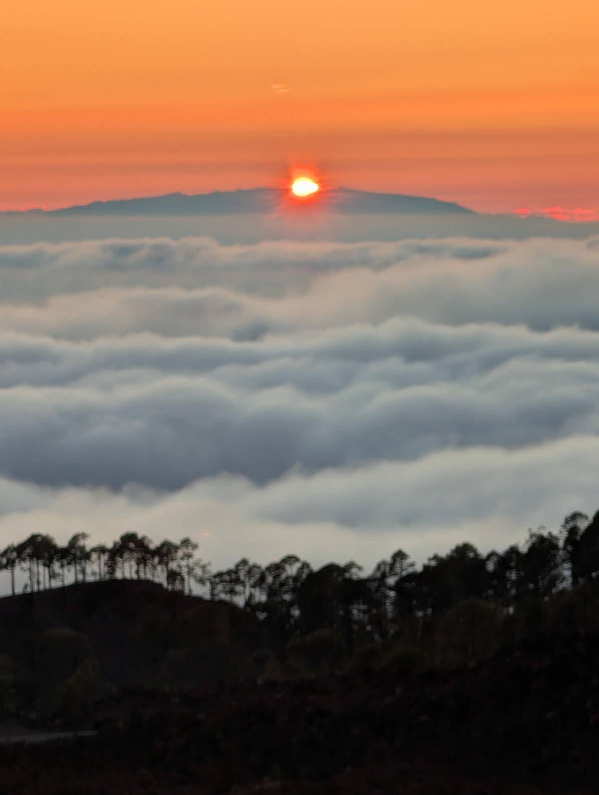 The sun setting behind an island above a sea of clouds