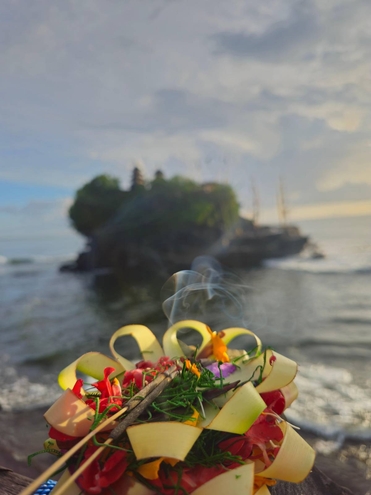 An offering with incense, Tanah Lot behind it