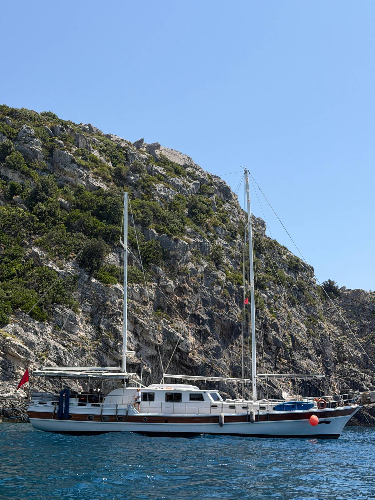 A sailing boat moored under the green hills of the coast