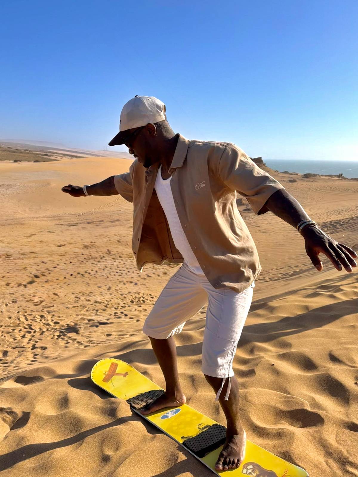 A rider standing on a yellow board on a sunlit dune