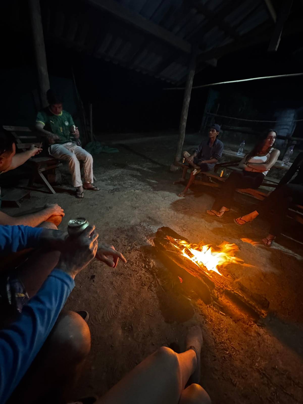 A campfire glowing under a village hut roof at night